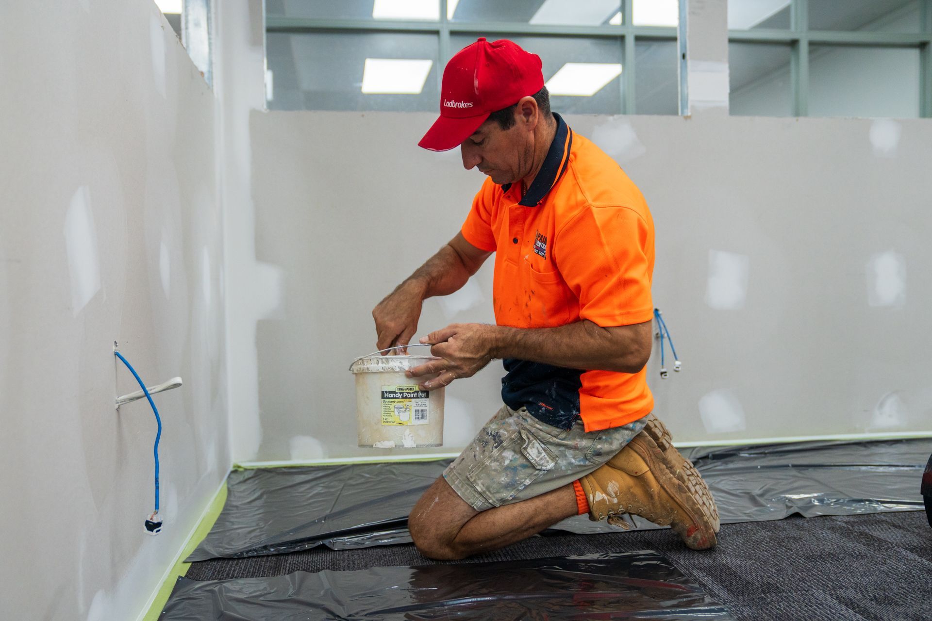 A man is kneeling down holding a bucket of paint.