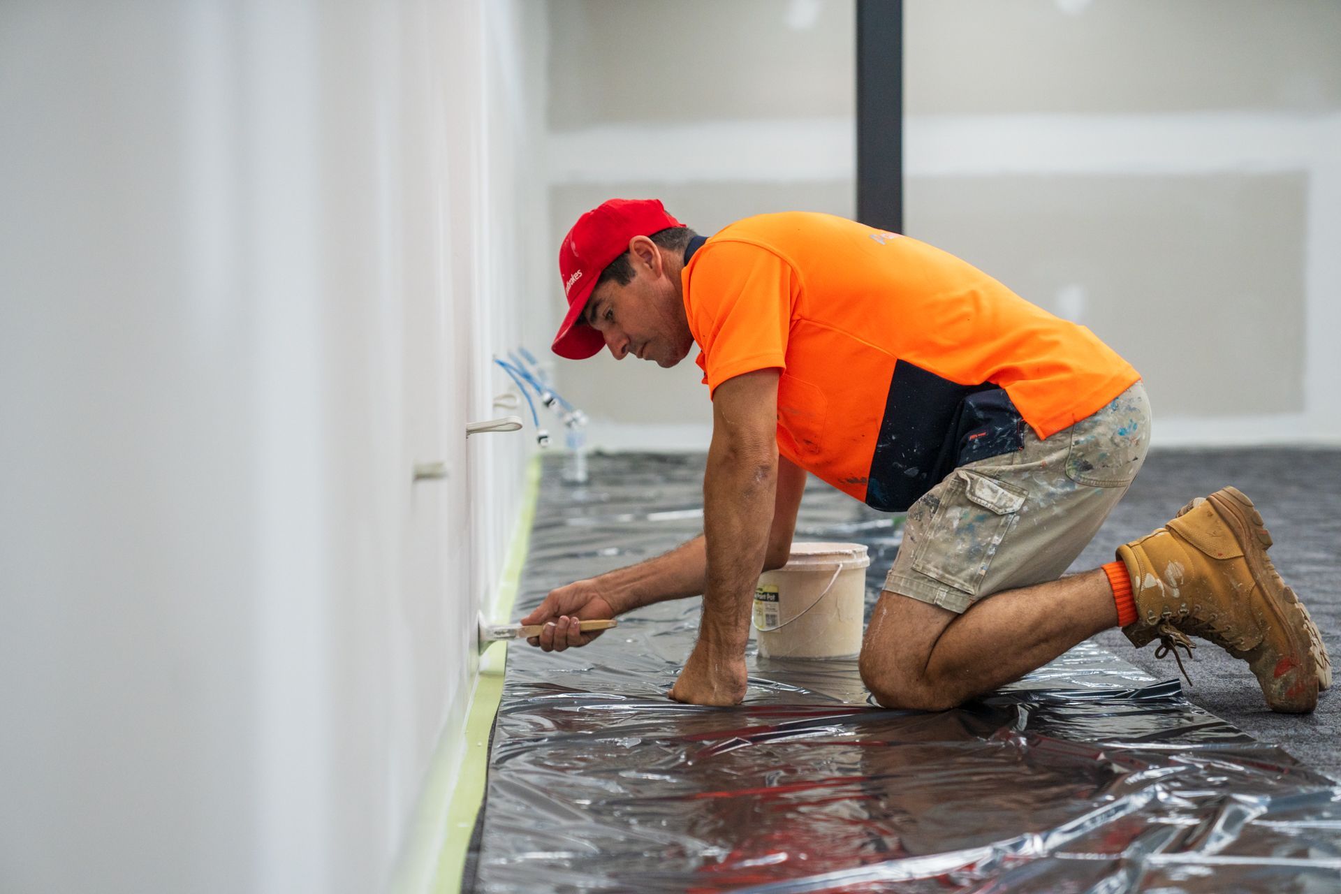 A man is kneeling down while painting a wall with a paint roller.