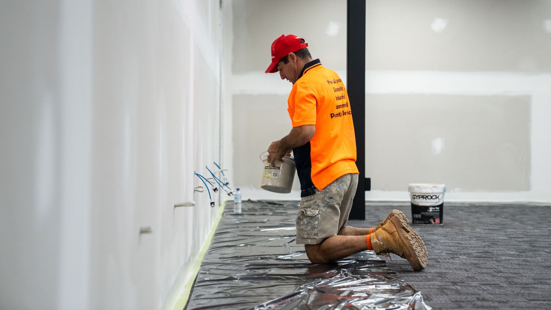 A man is kneeling down while painting a wall.