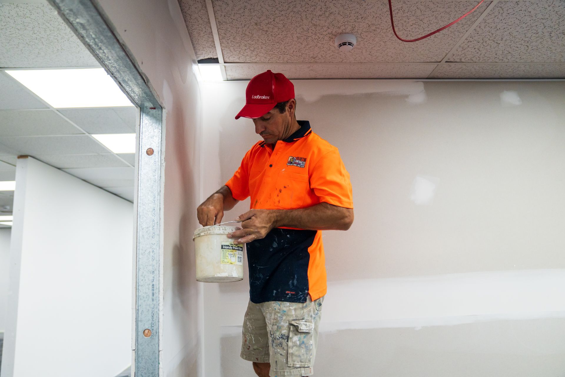 A man is standing on a wall holding a bucket of paint.