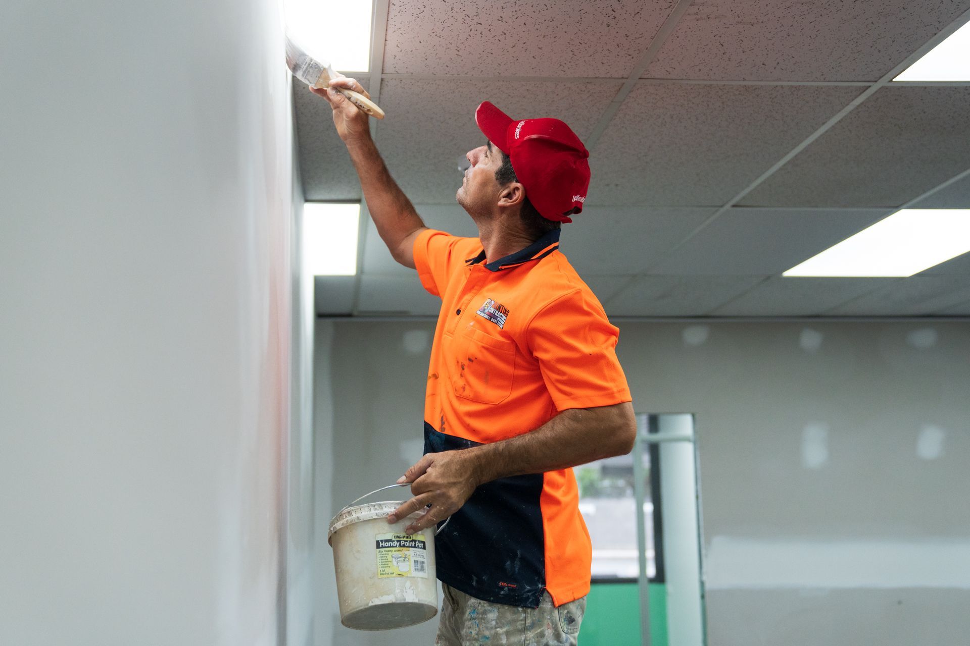 A man is painting a wall with a brush and a bucket of paint.