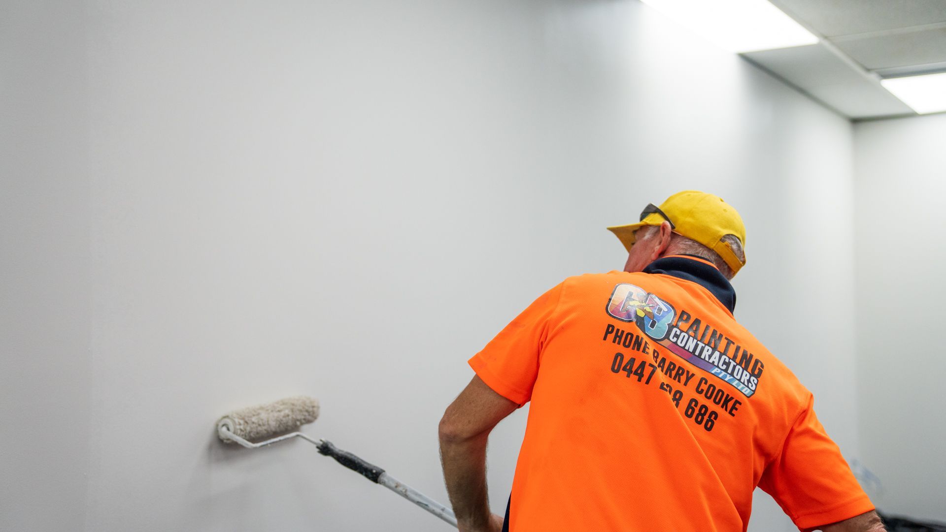 A man in an orange shirt is painting a wall with a roller.