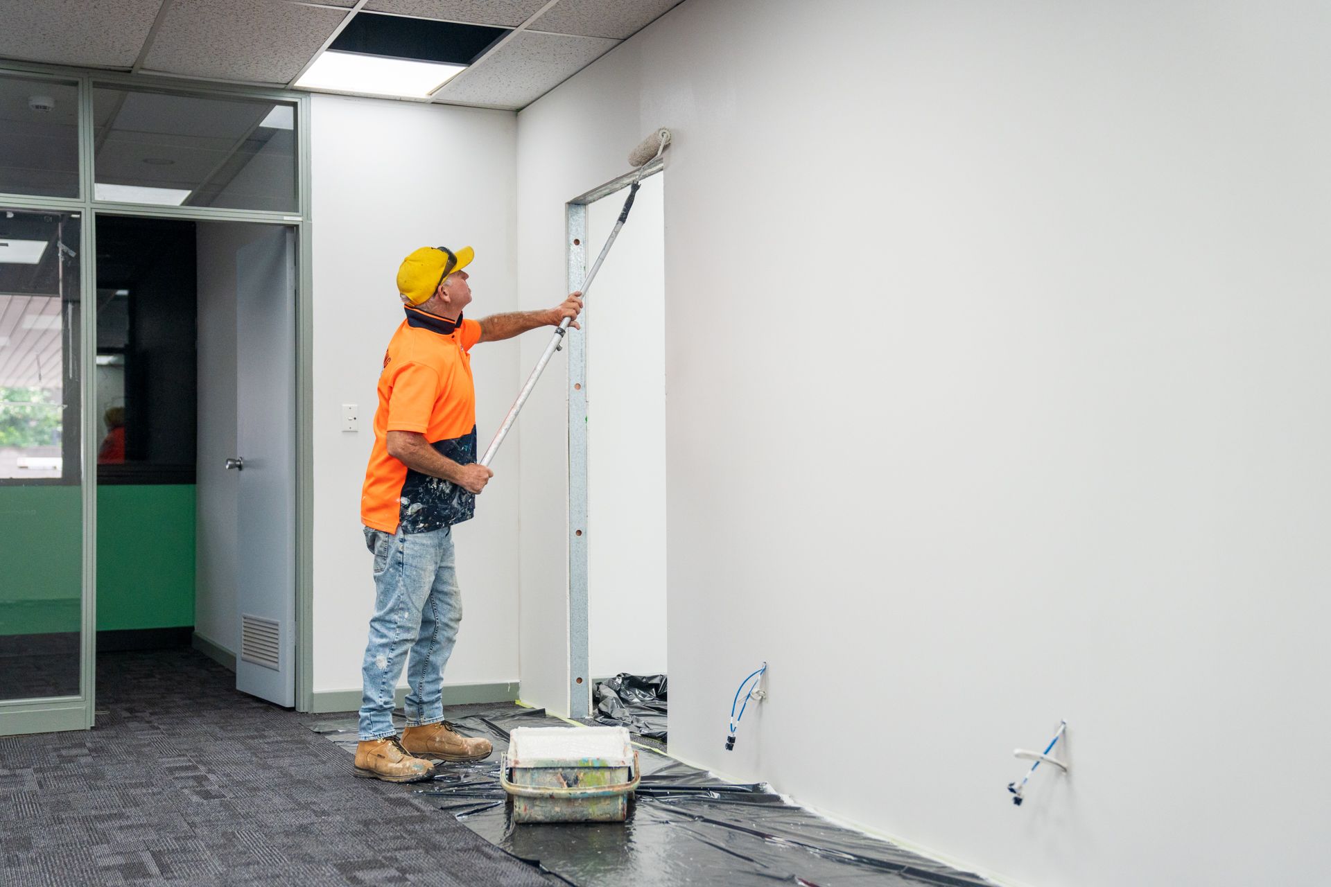 A man is painting a wall with a roller in an empty room.