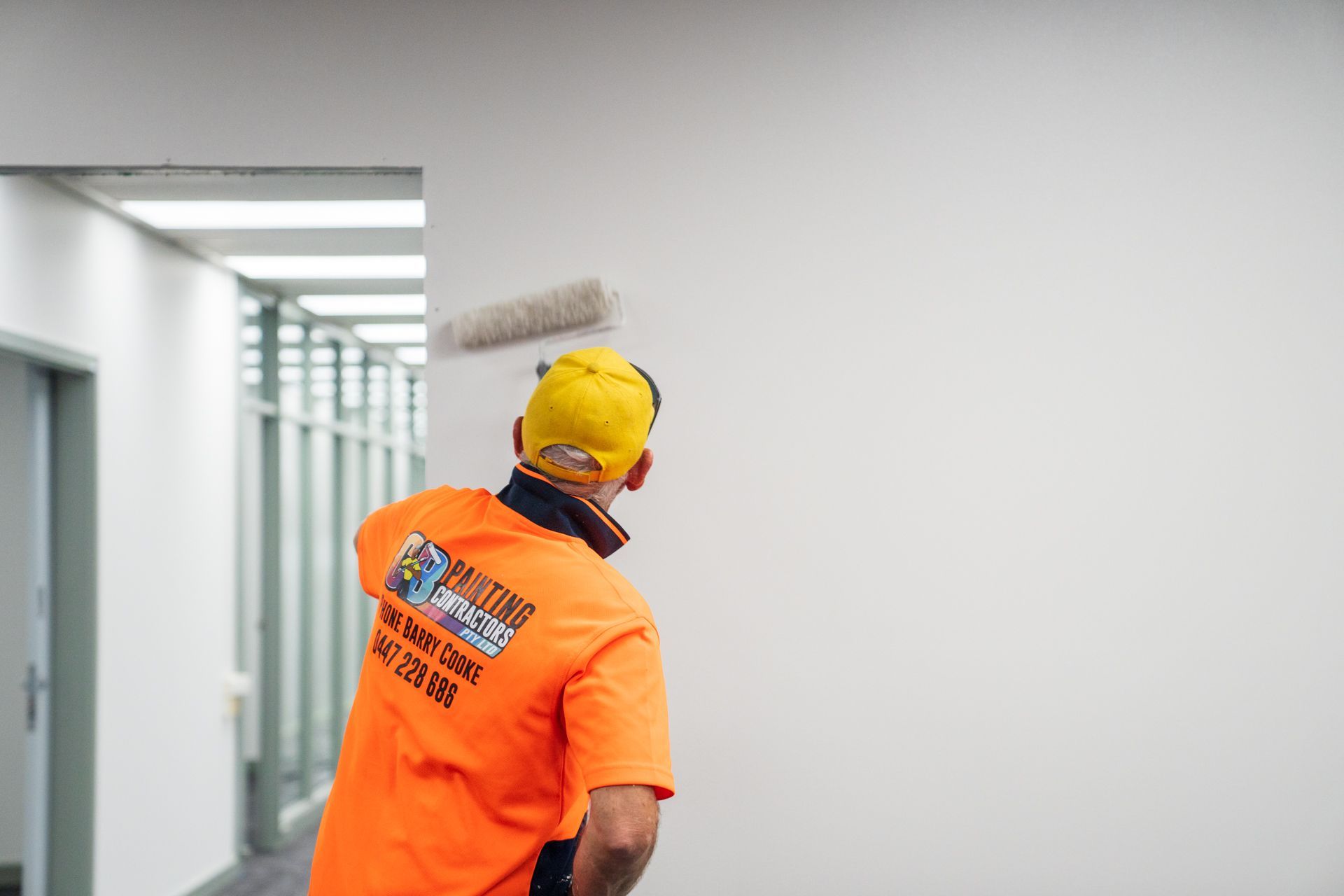 A man in an orange shirt is painting a wall with a roller.