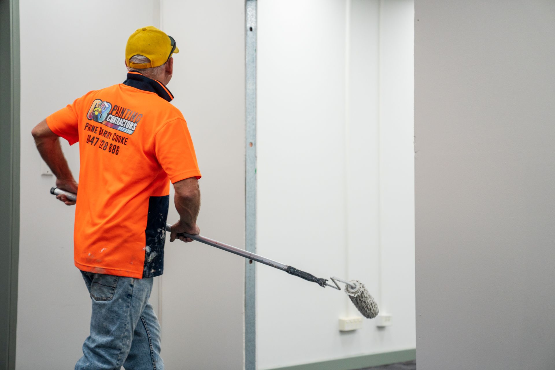 A man in an orange shirt is cleaning a wall with a mop.