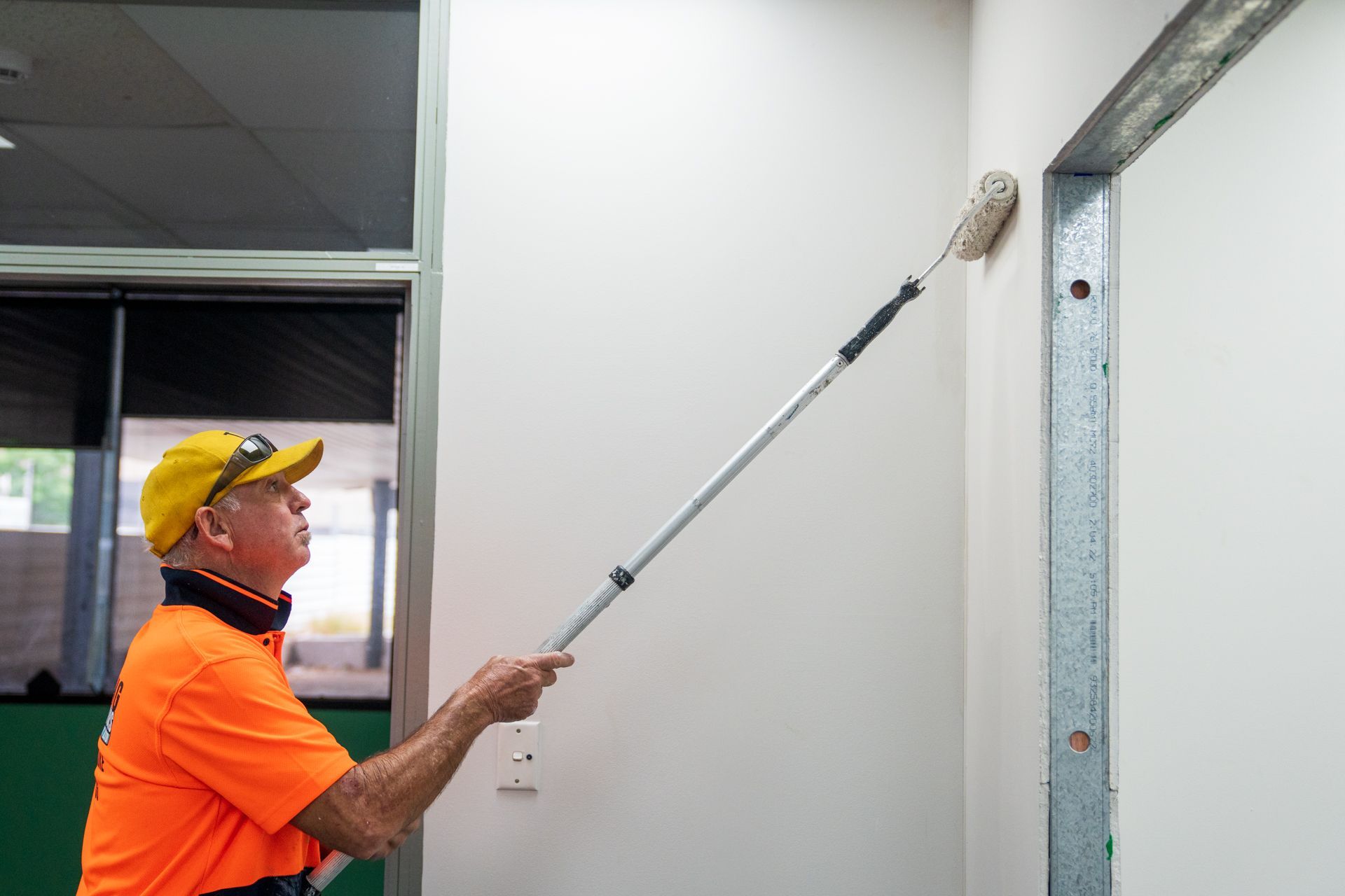 A man is painting a wall with a long paint roller.