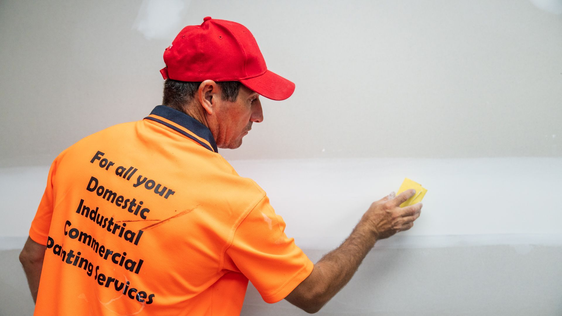 A man in an orange shirt is cleaning a wall with a sponge.