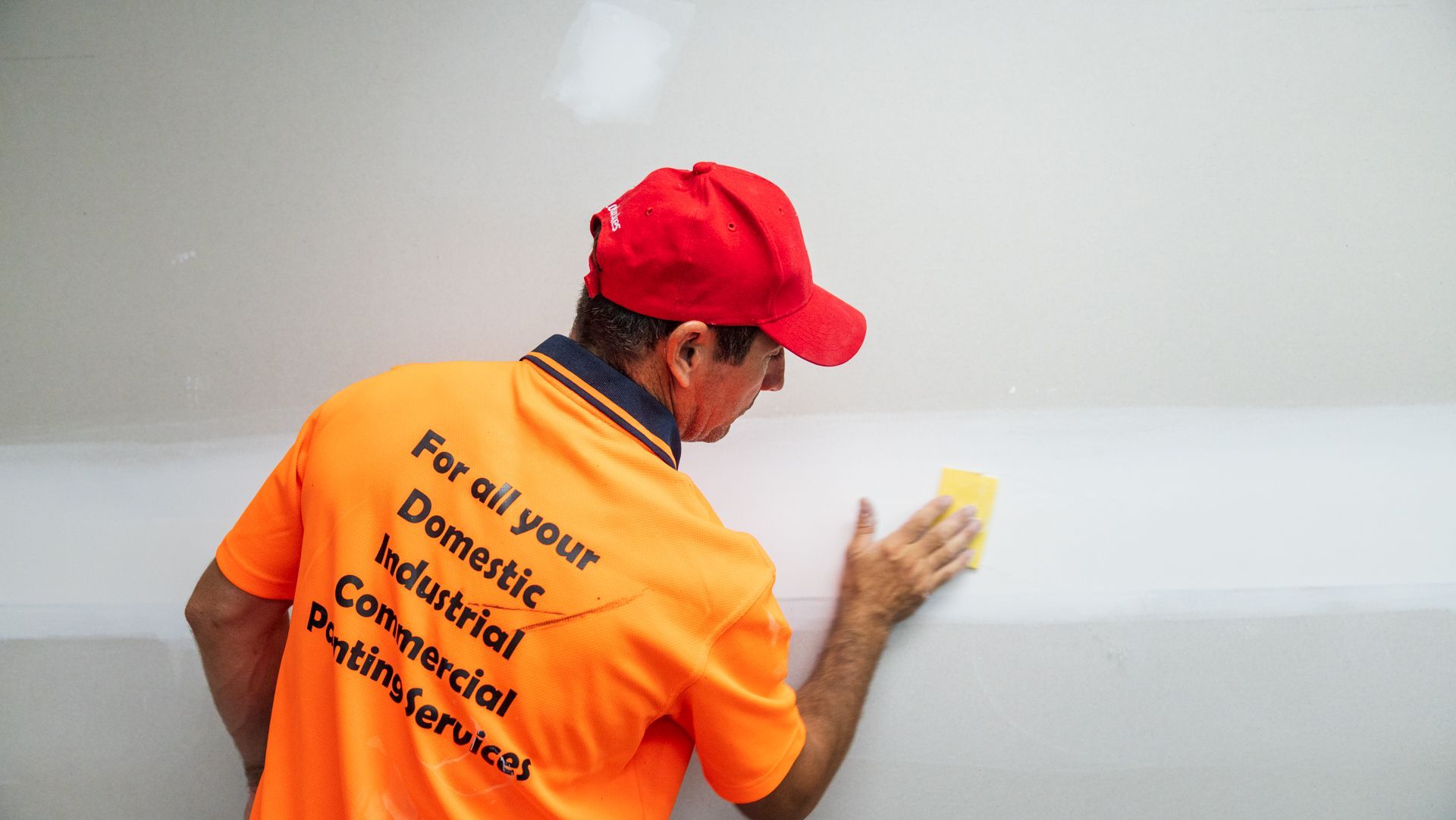 A man in an orange shirt is cleaning a wall with a sponge.