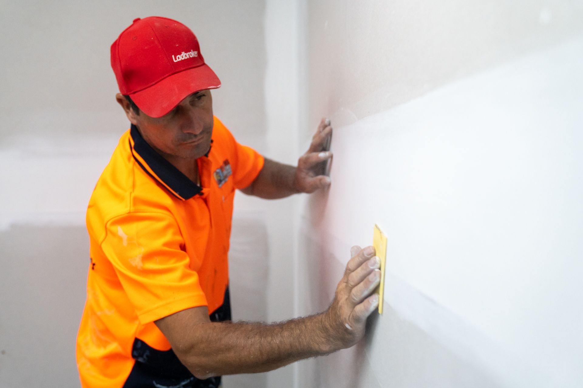 A man in an orange shirt and red hat is cleaning a wall with a sponge.