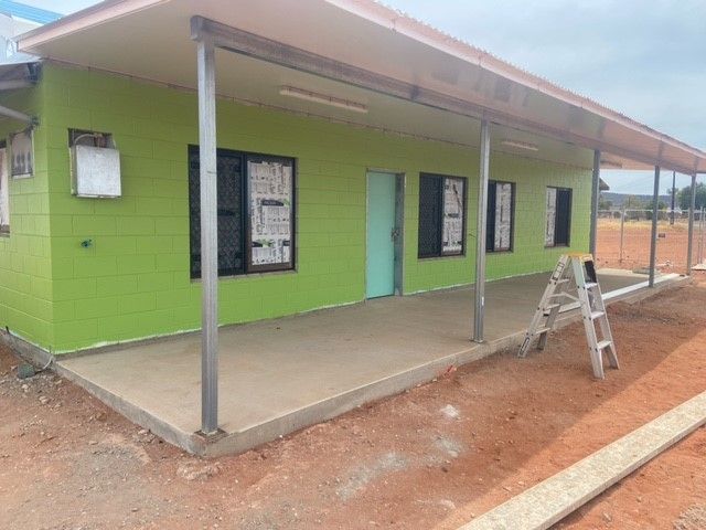 A green house with a porch and a ladder in front of it.