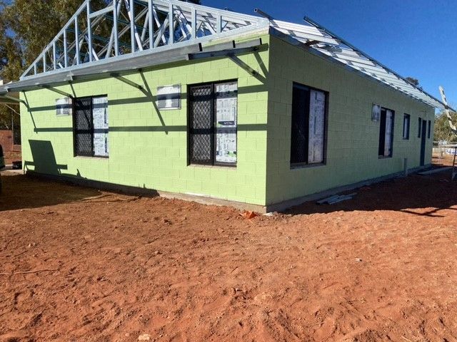 A green house is sitting in the middle of a dirt field.