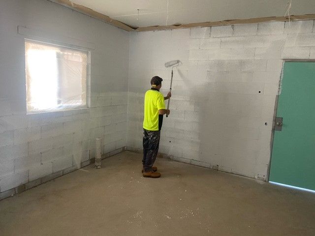 A man is painting a wall with a roller in a room.
