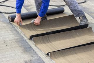 A worker laying fown flat roofing on top of a building