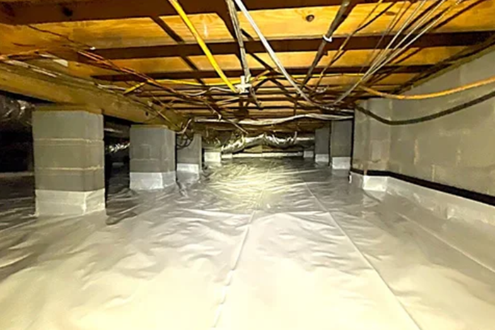 A crawl space with concrete piers, exposed wooden joists, and a white vapor barrier covering the ground.