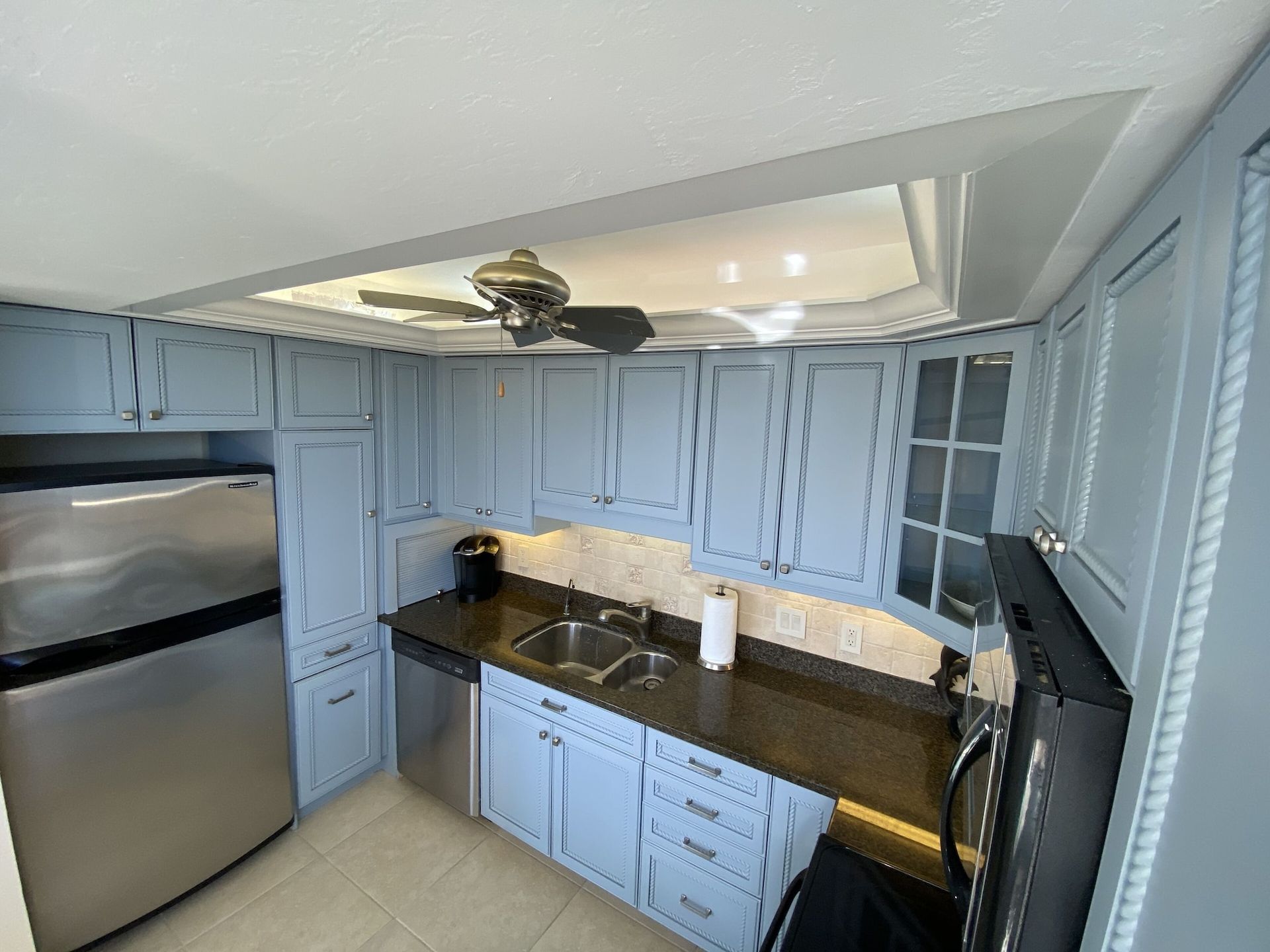 A kitchen with blue cabinets , stainless steel appliances and a ceiling fan.