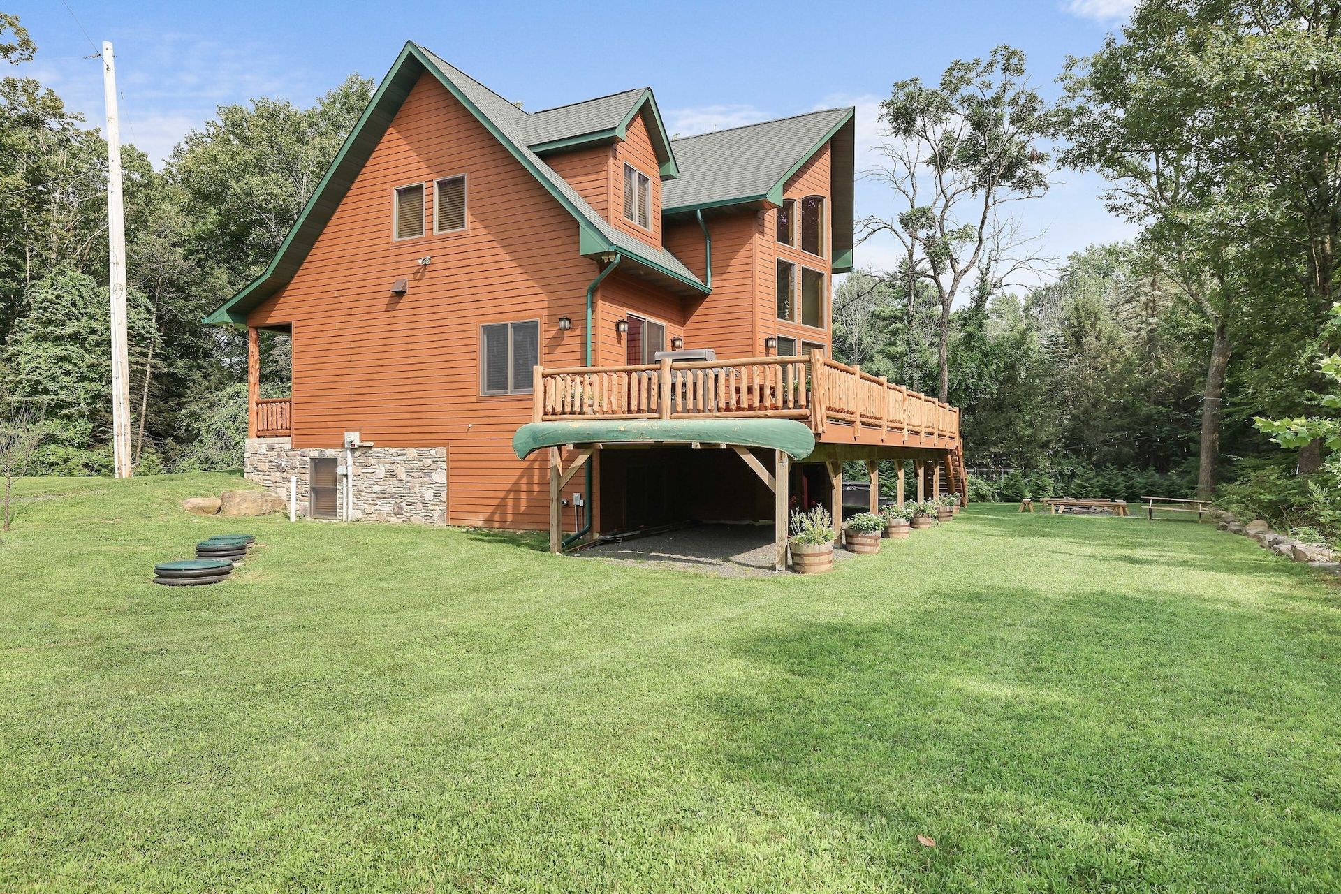 A large wooden house with a large deck is surrounded by trees.