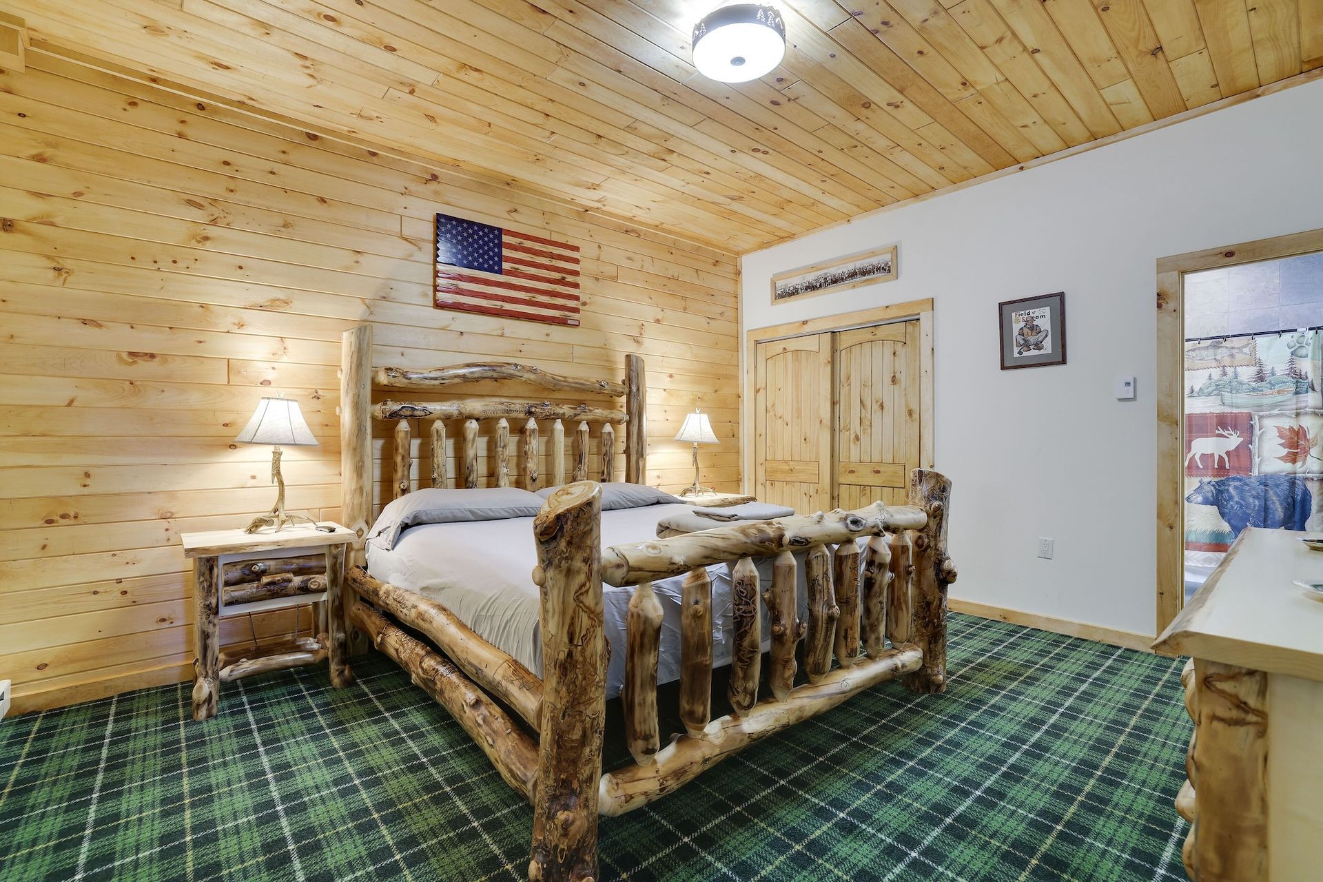A bedroom with a log bed , dresser , nightstand and american flag on the wall.