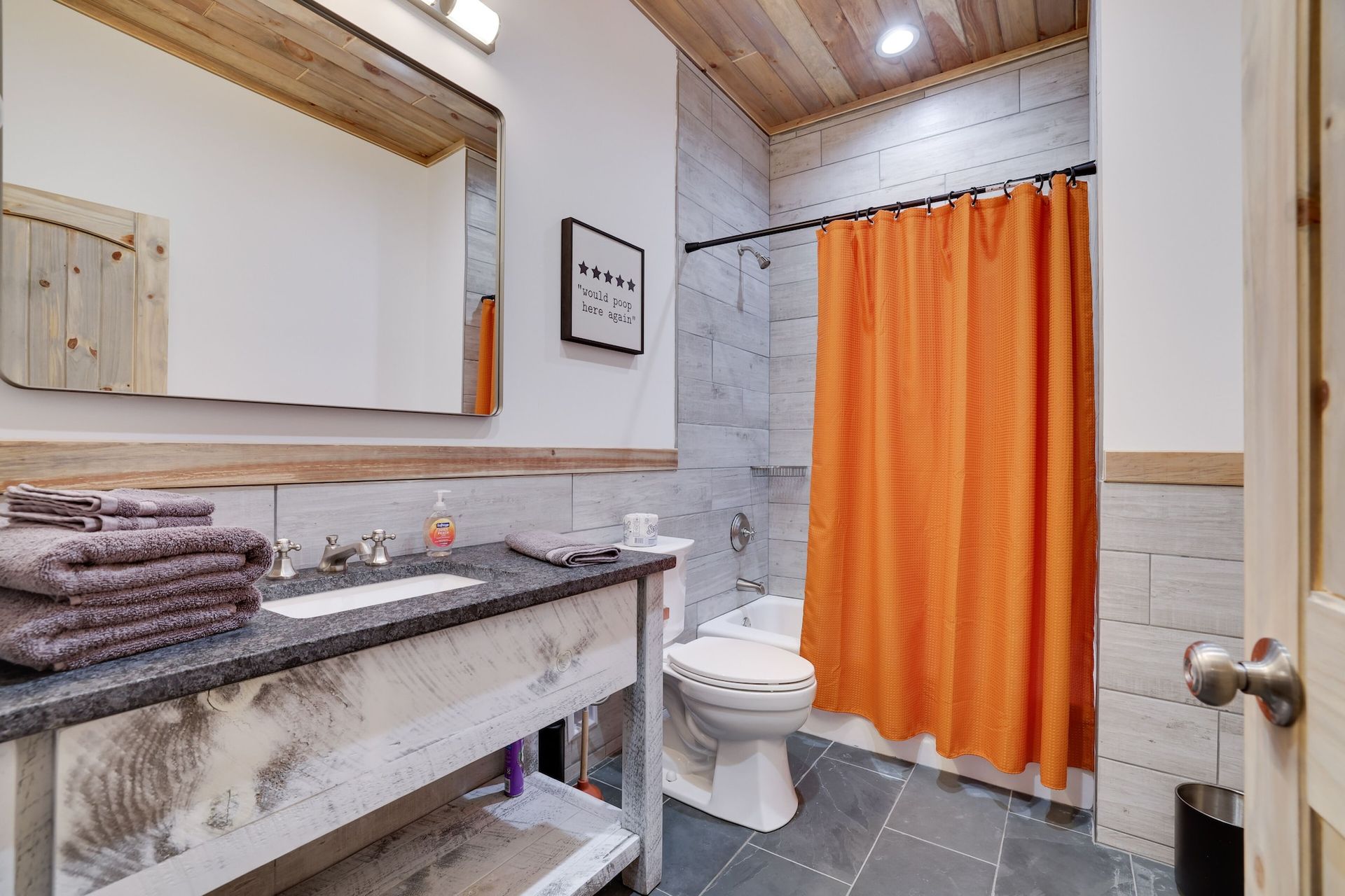A bathroom with a toilet , sink , mirror and orange shower curtain.