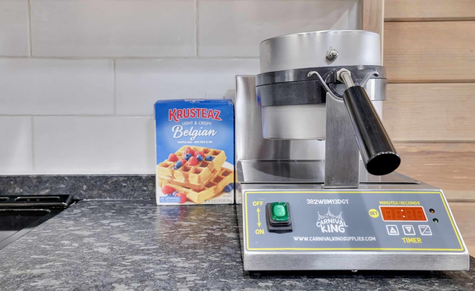 A waffle maker is sitting on a counter next to a box of waffle mix.