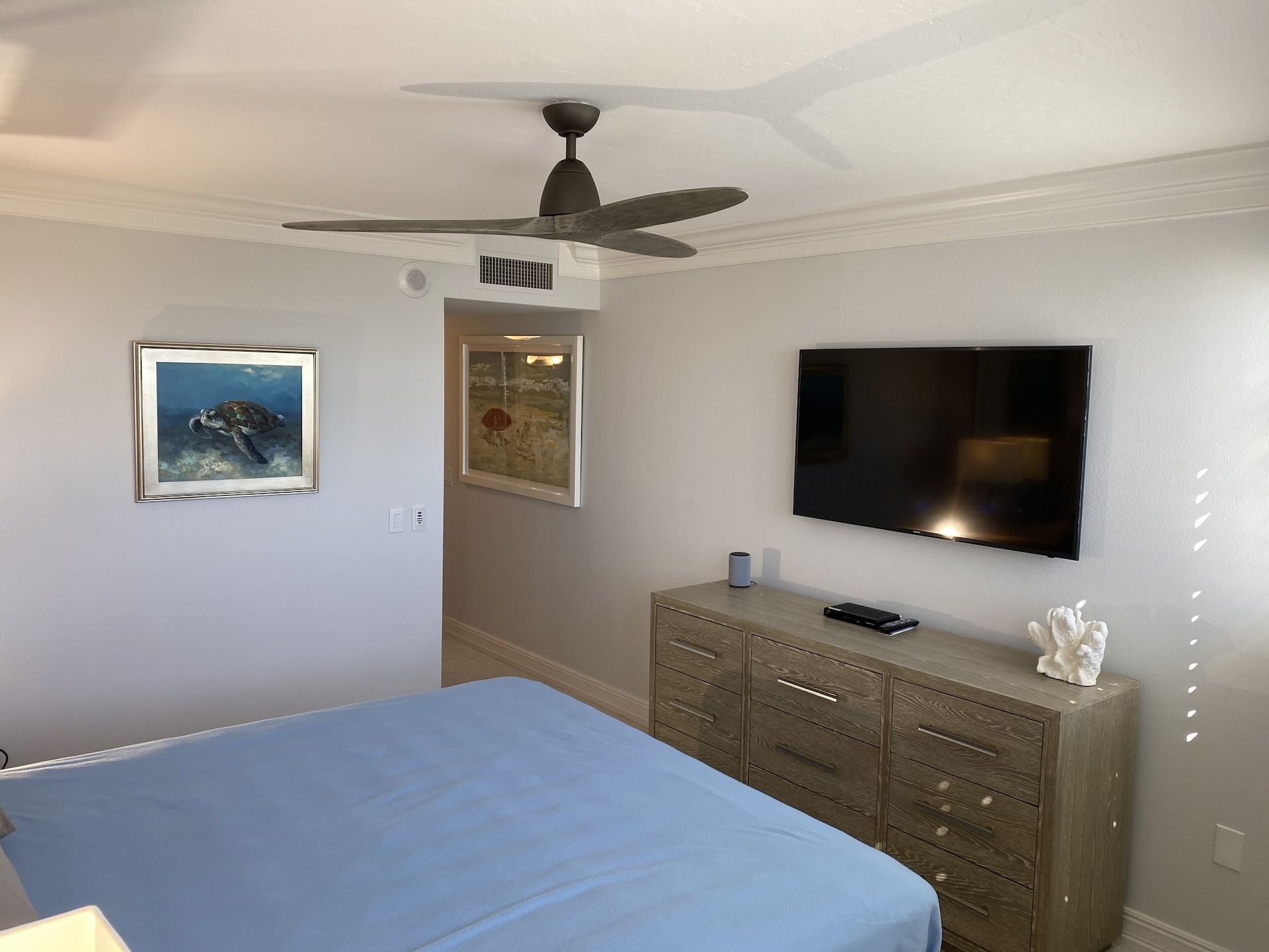 A bedroom with a bed , dresser , television and ceiling fan.