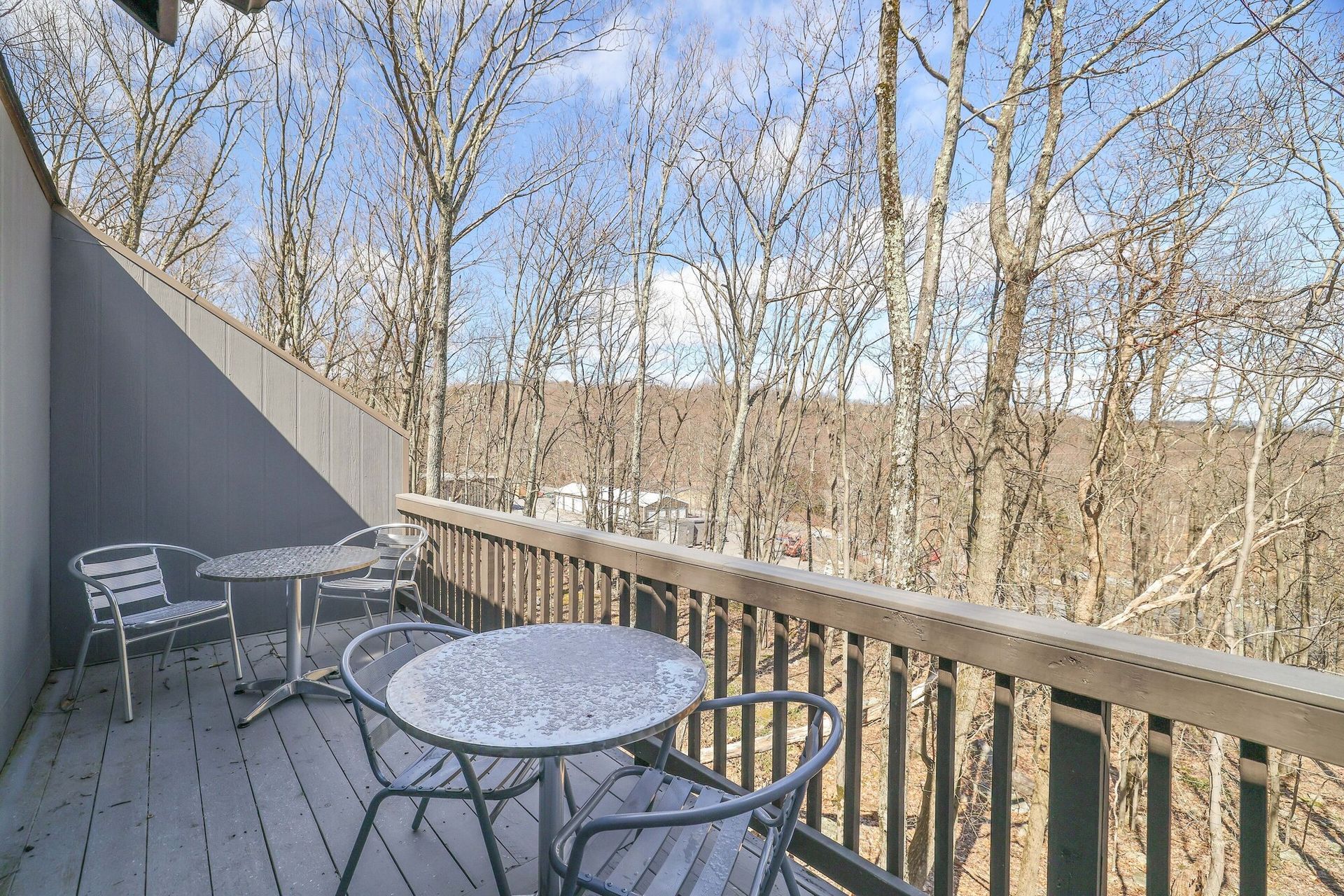 A balcony with a table and chairs and trees in the background.