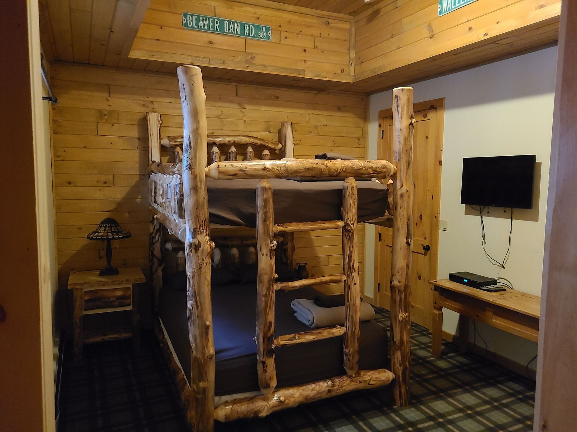 A bedroom with a bunk bed made of logs and a flat screen tv.
