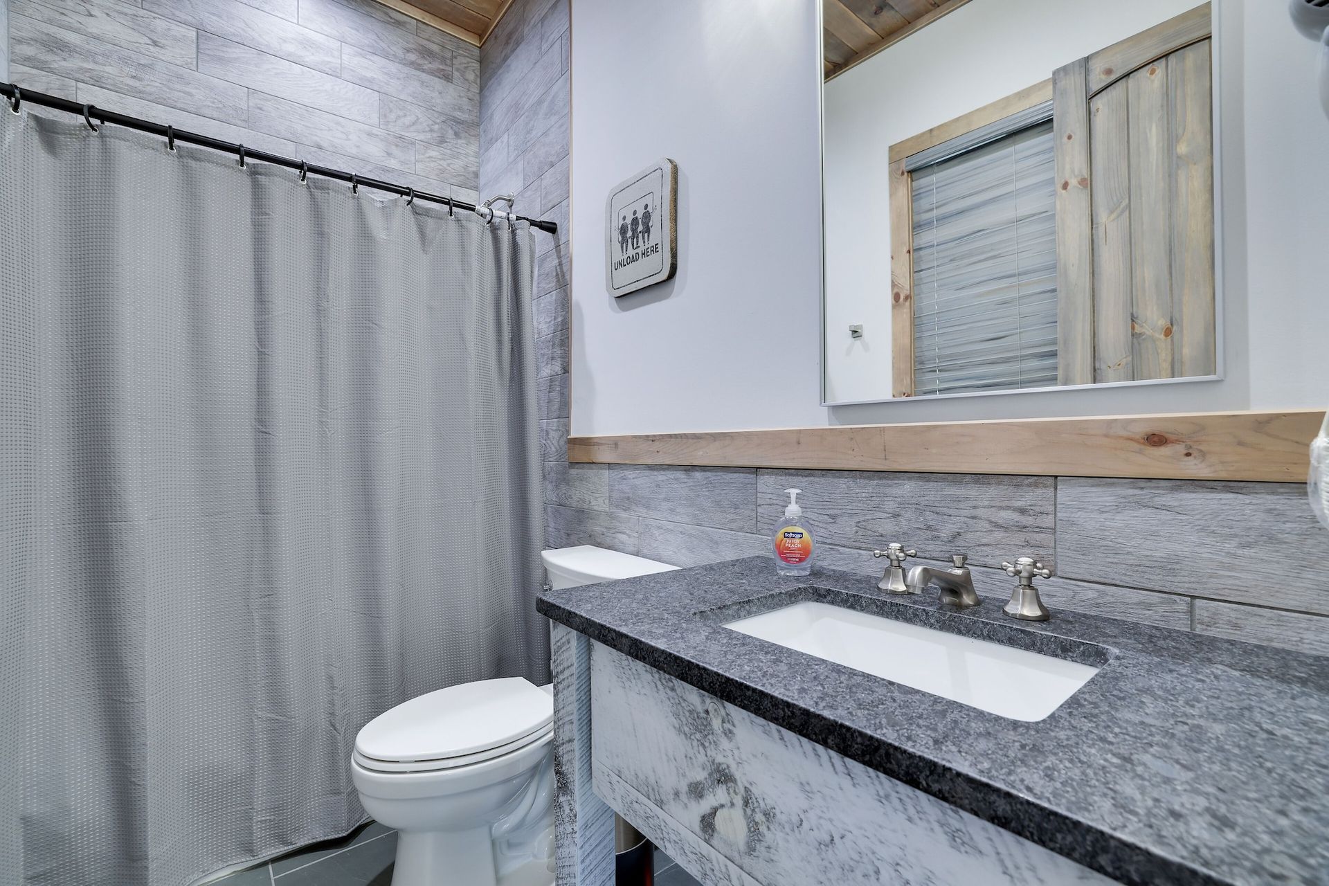 A bathroom with a toilet , sink , mirror and shower curtain.