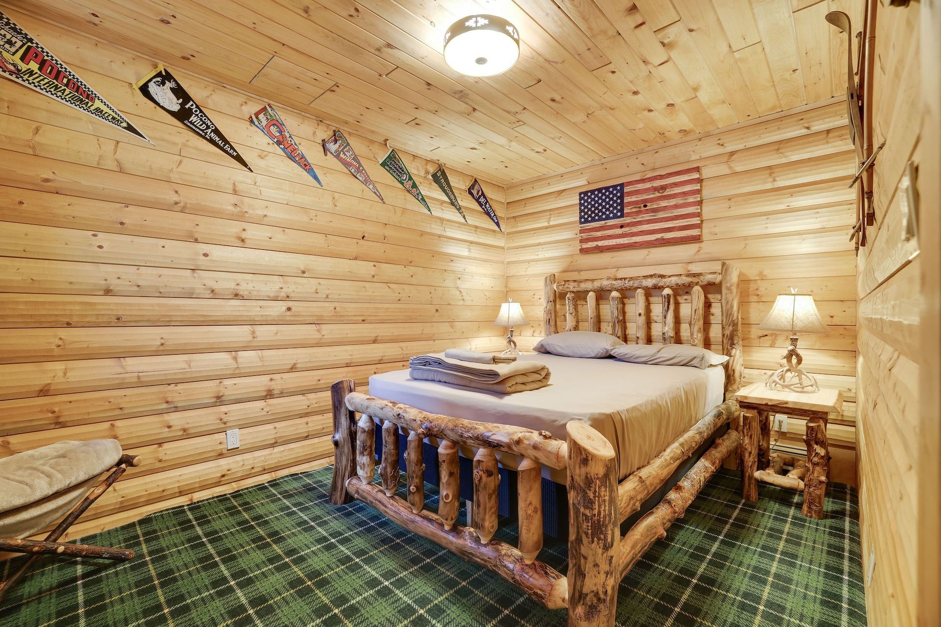 A bedroom in a log cabin with a bed , lamps , and an american flag on the wall.
