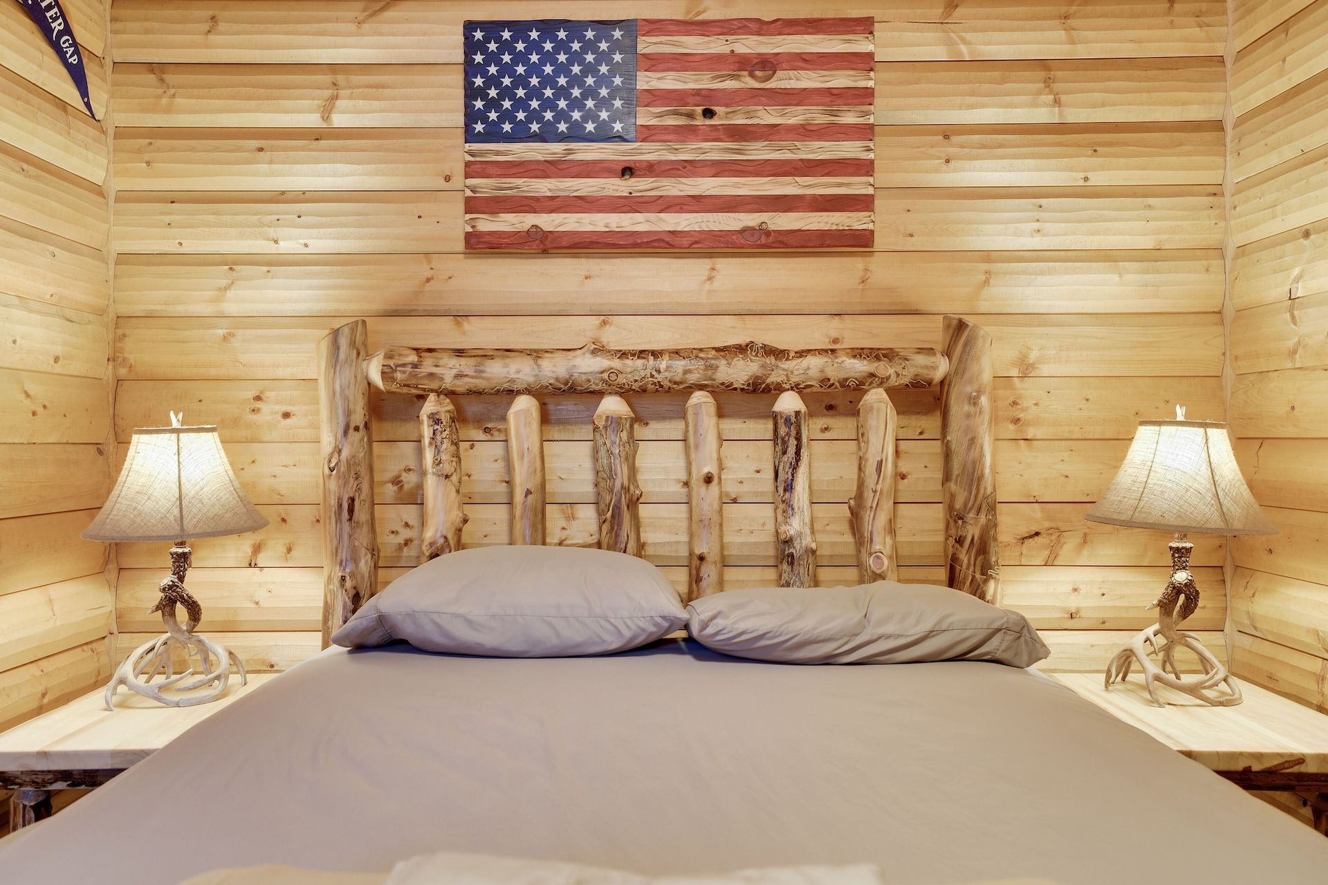 A bedroom with a bed , lamps and an american flag on the wall.