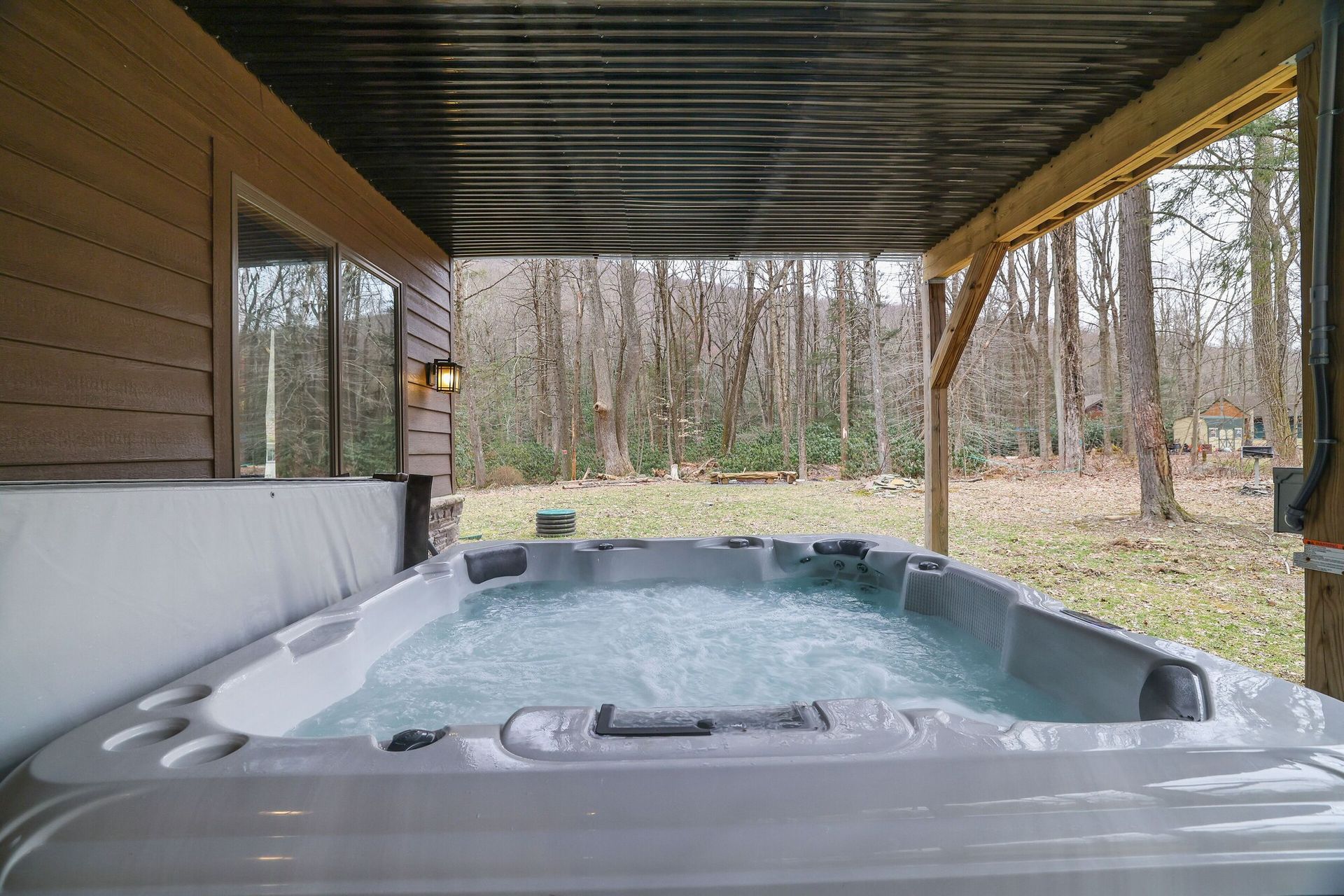 A hot tub is sitting under a canopy on the side of a house.