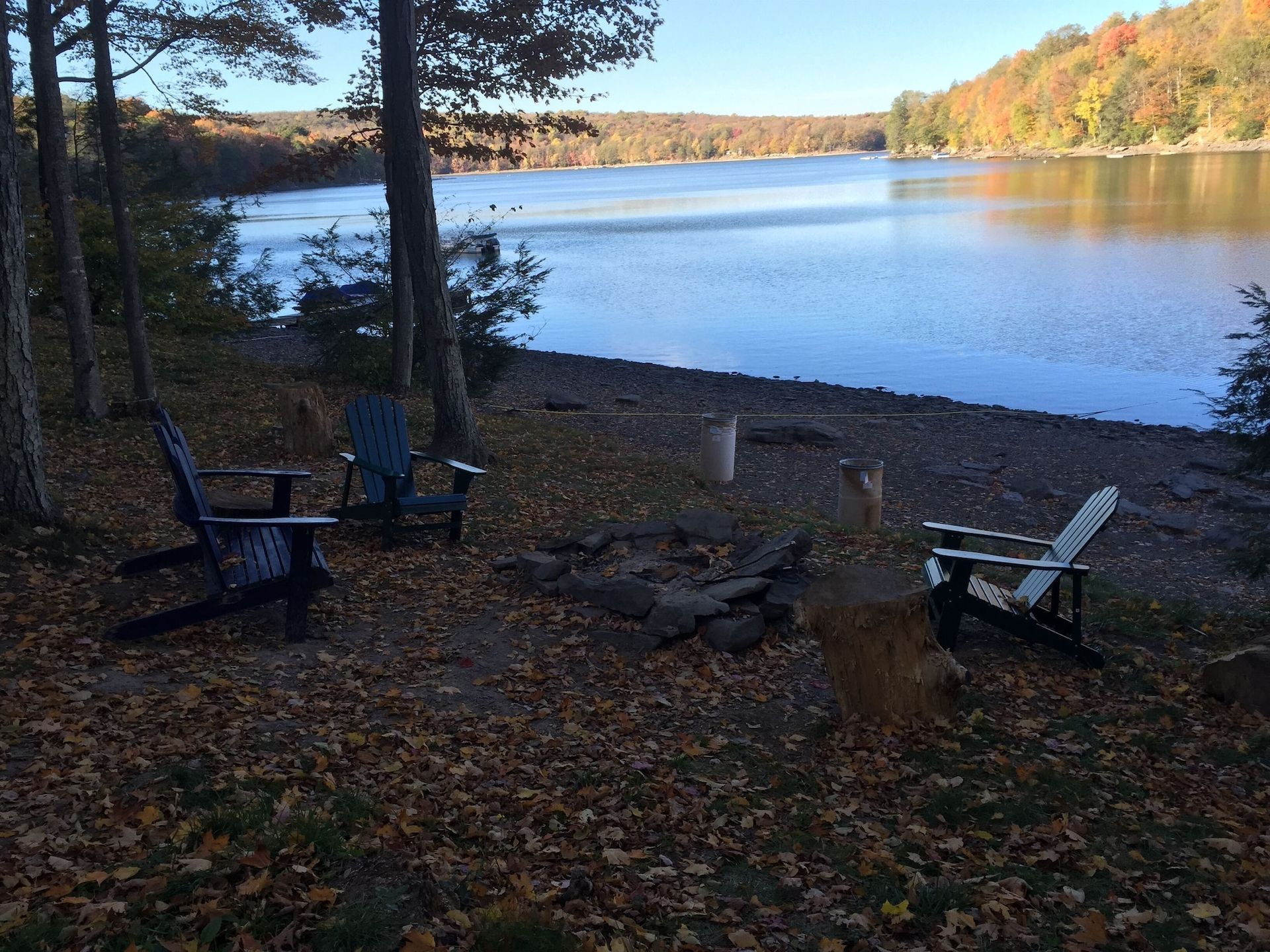 A group of chairs are sitting next to a fire pit on the shore of a lake.