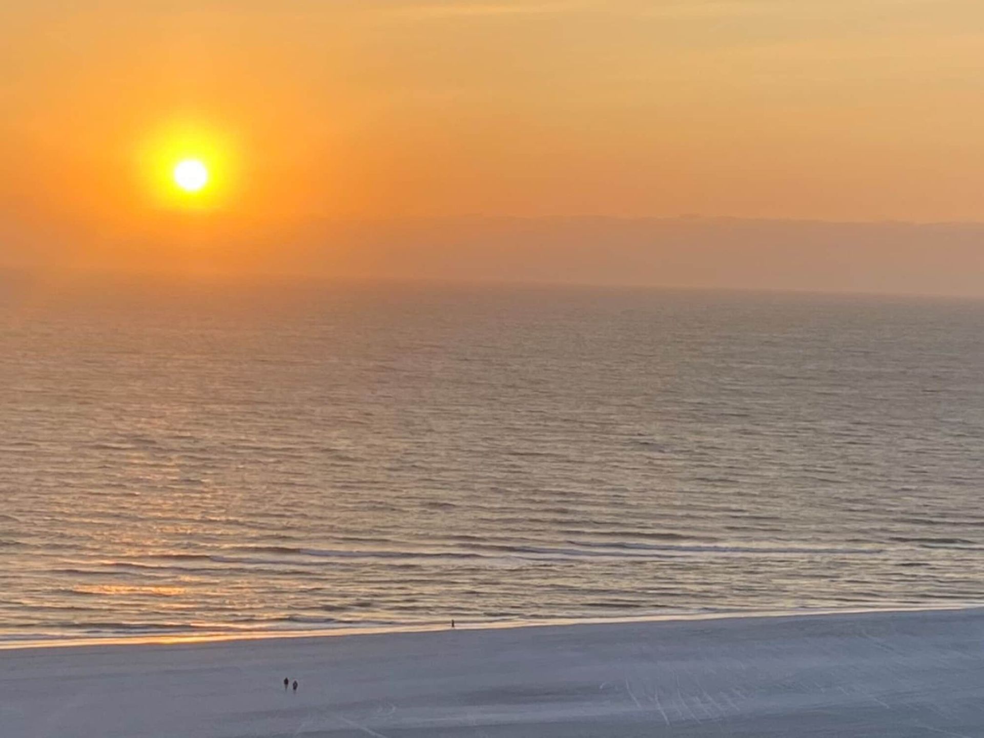 The sun is setting over the ocean and a couple is walking on the beach.