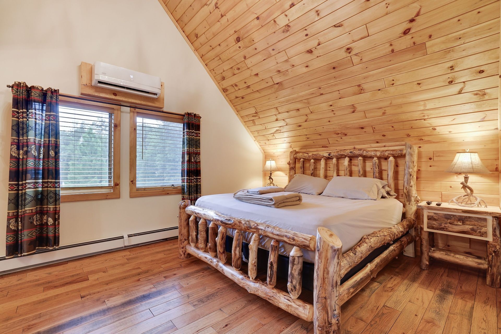 A bedroom with a log bed , two windows and a wooden ceiling.