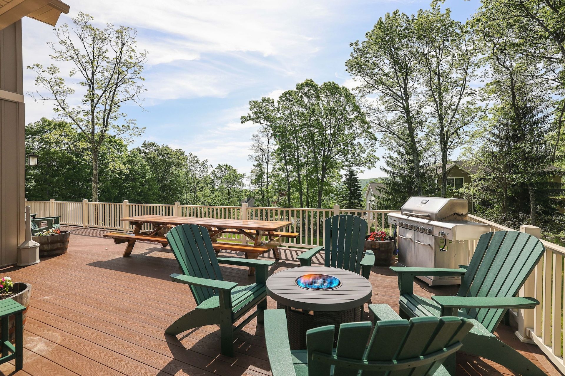 A deck with green chairs , a table and a grill.