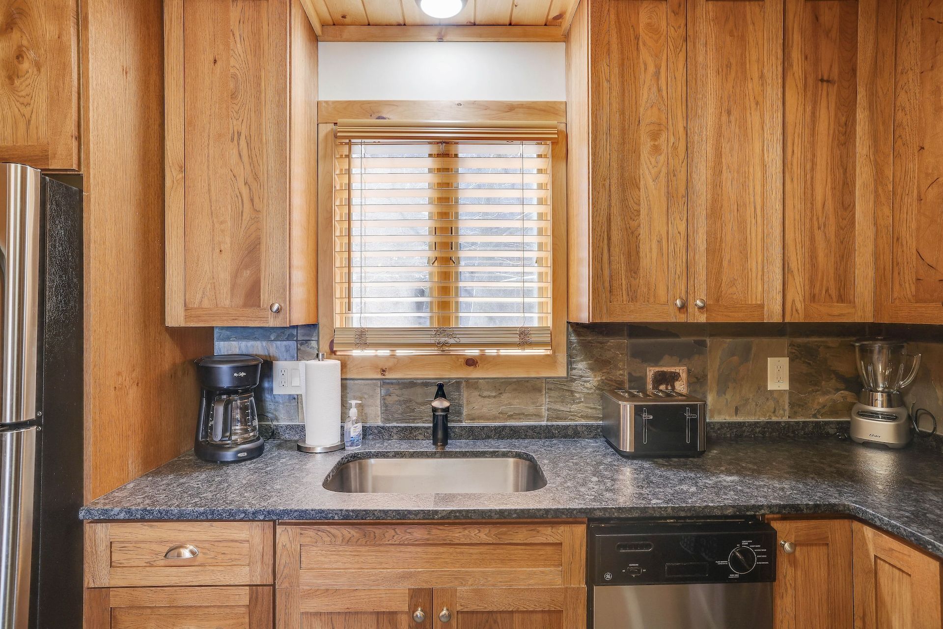 A kitchen with wooden cabinets , stainless steel appliances , a sink , and a window.