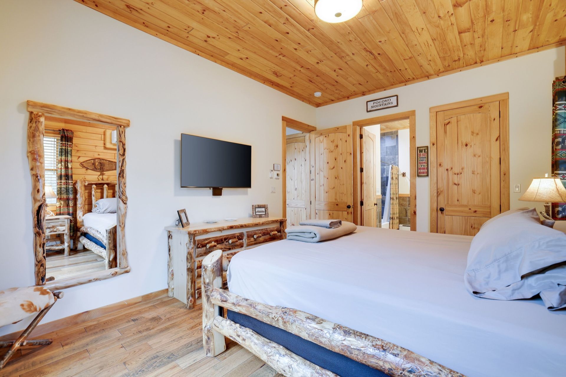 A bedroom with a bed , television , mirror and wooden ceiling.