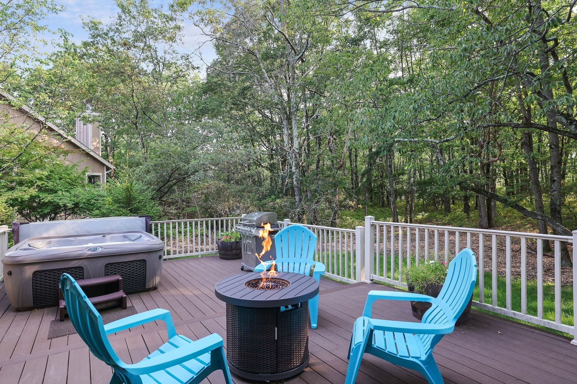 A deck with blue chairs and a fire pit and a hot tub.