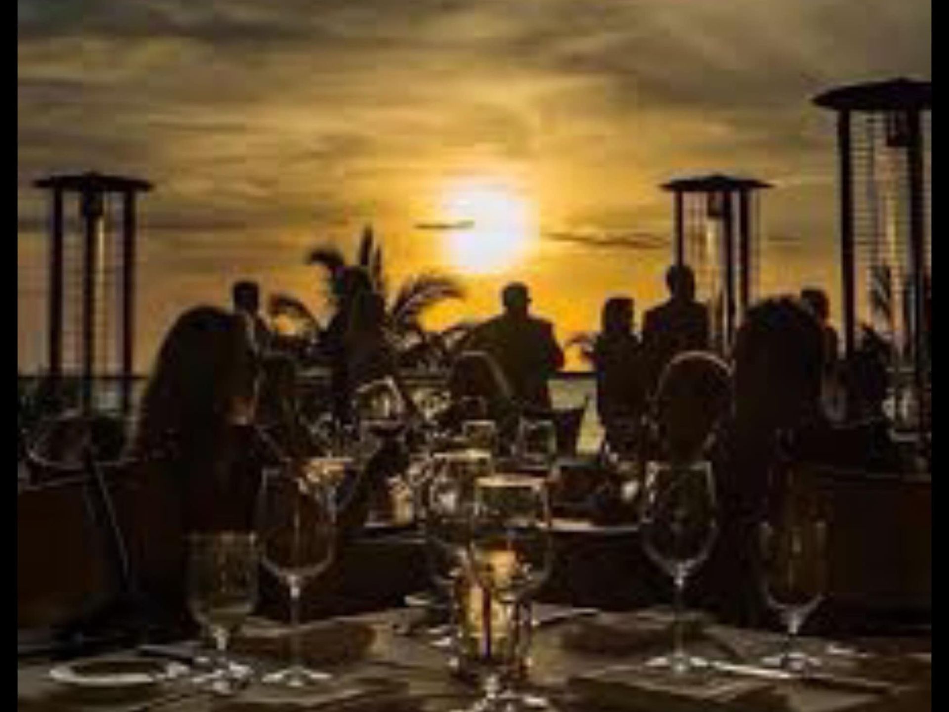 A group of people are sitting at a table with a sunset in the background.