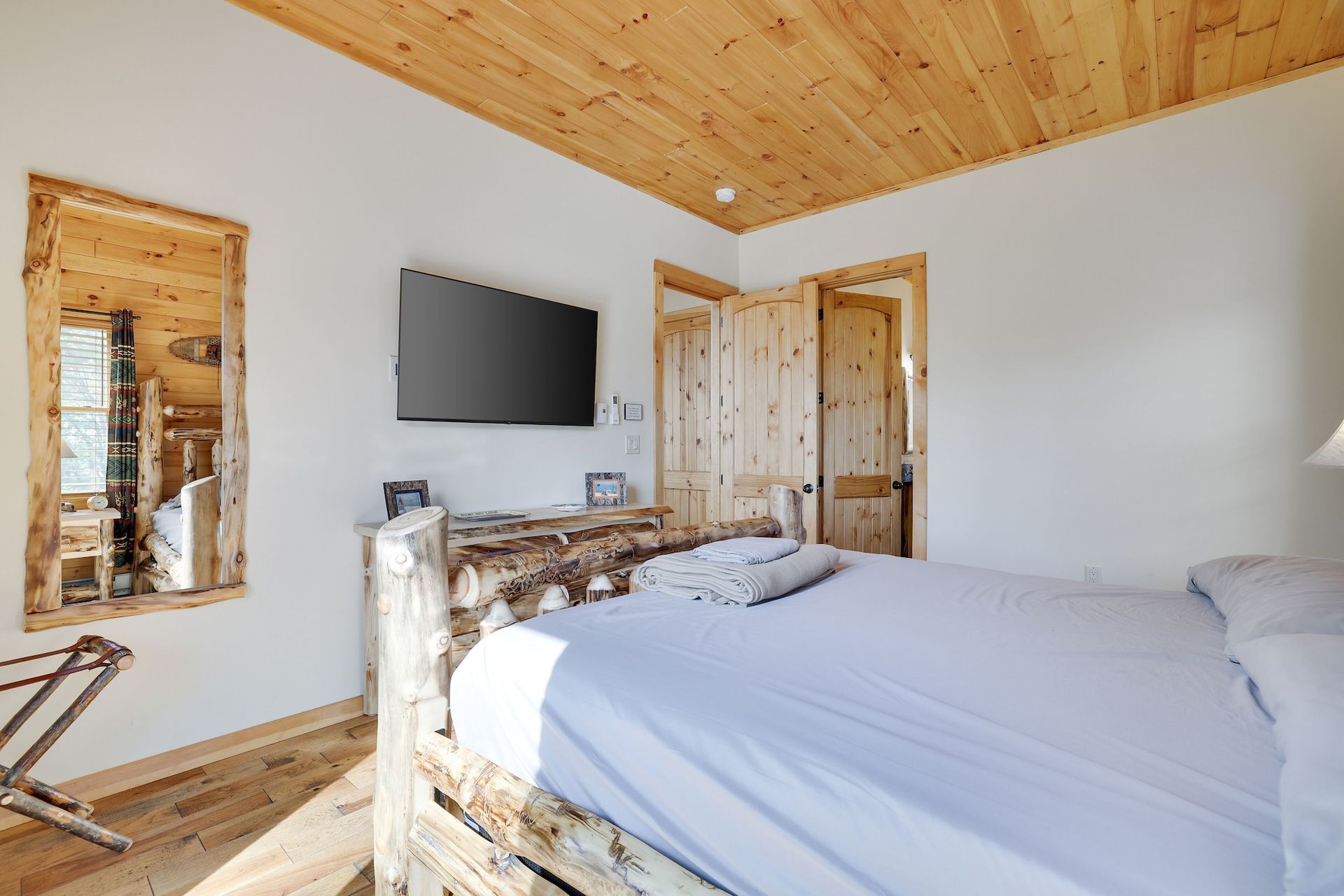 A bedroom with a bed , television , mirror and wooden ceiling.