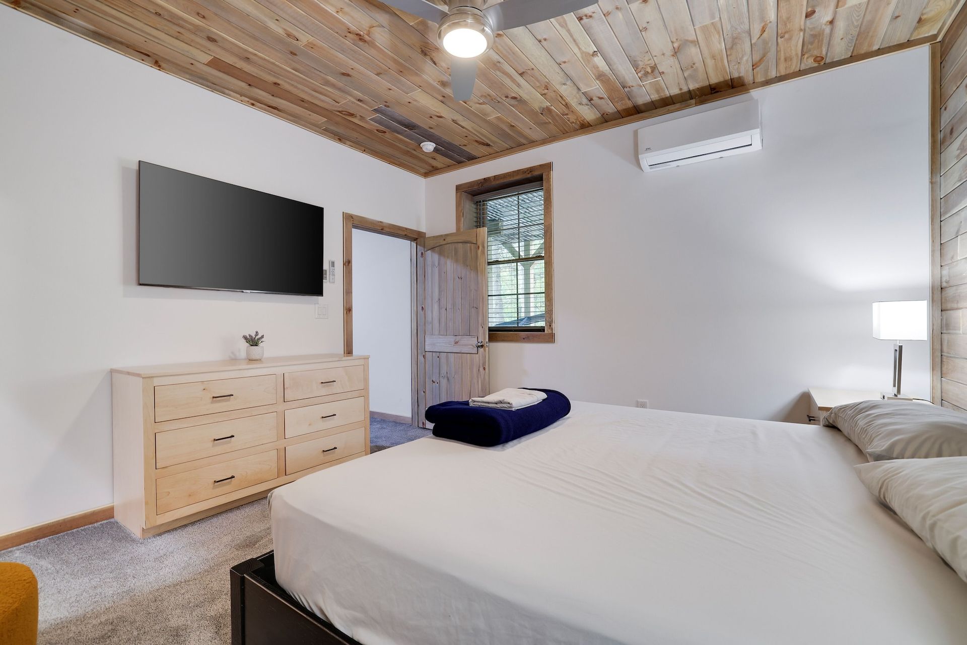 A bedroom with a bed , dresser , television and wooden ceiling.
