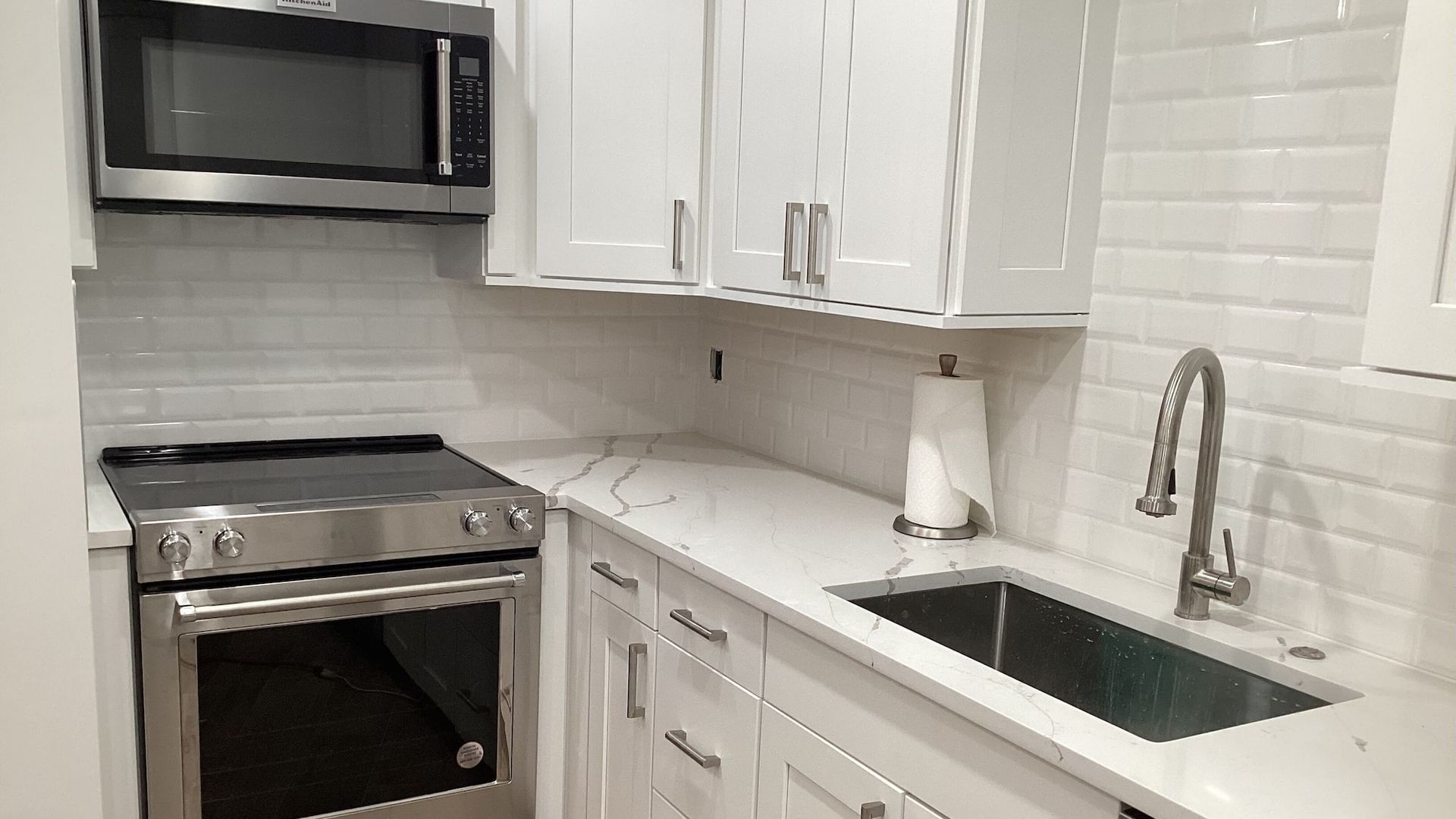 A kitchen with white cabinets , stainless steel appliances , a sink , and a microwave.
