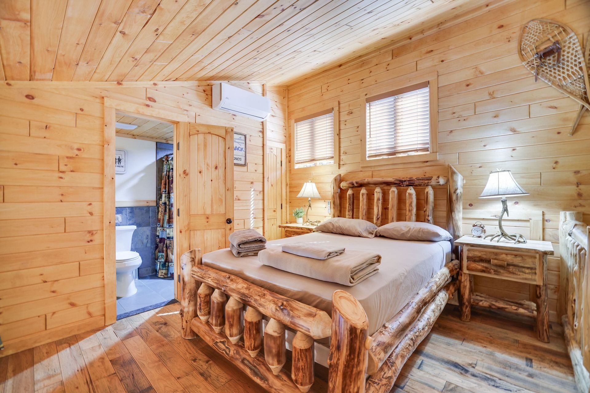 A bedroom in a log cabin with a log bed , nightstands , lamps and a toilet.