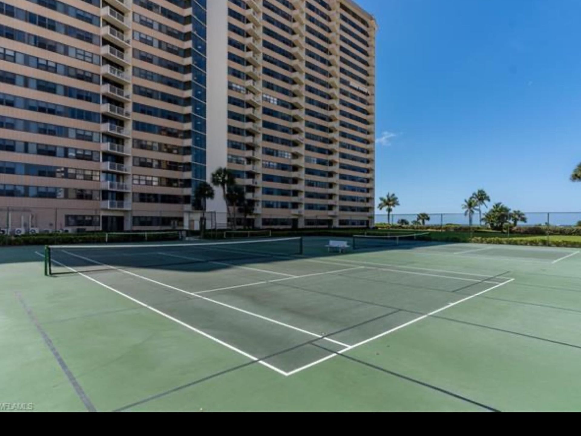 There is a tennis court in front of a tall building.