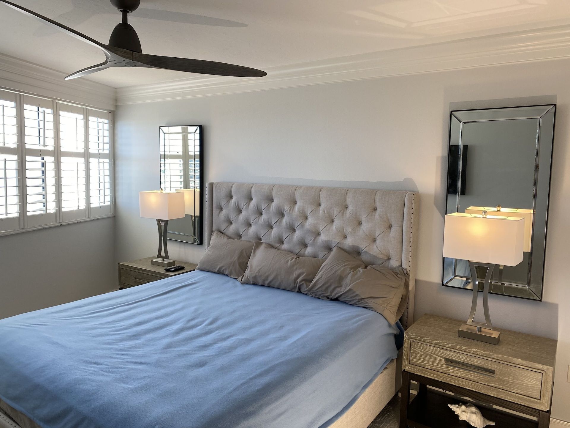 A bedroom with a bed , two lamps , two mirrors and a ceiling fan.