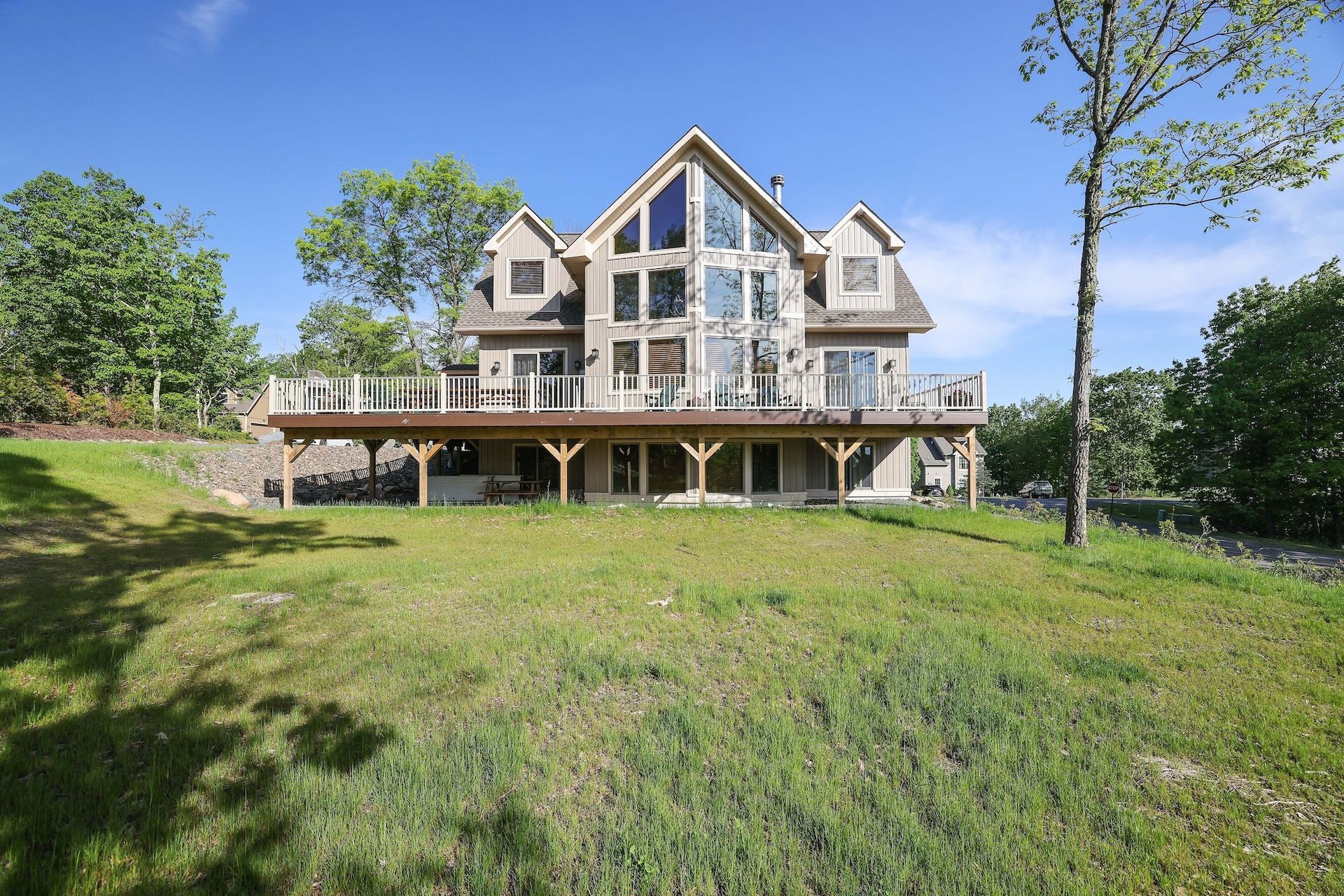 A large house with a large deck is sitting on top of a grassy hill.