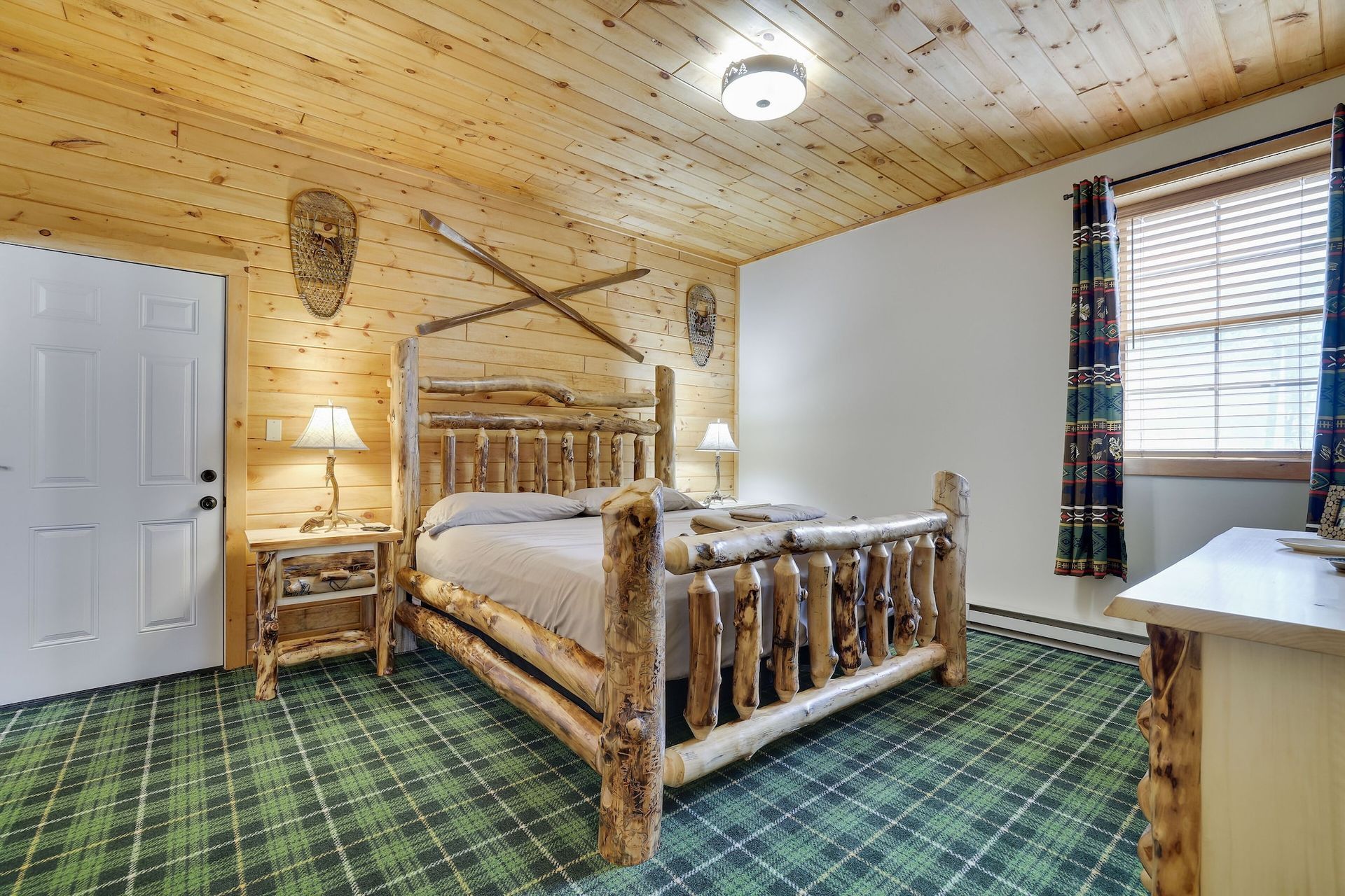A bedroom with a log bed , dresser , nightstand and window.