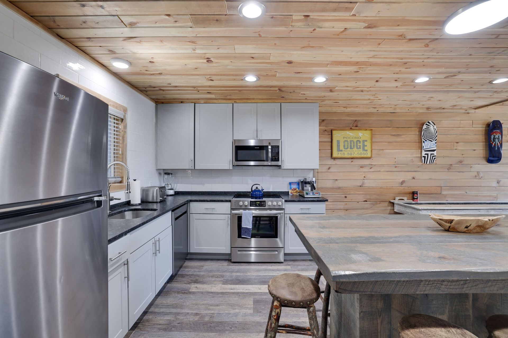 A kitchen with stainless steel appliances , white cabinets and a wooden ceiling.