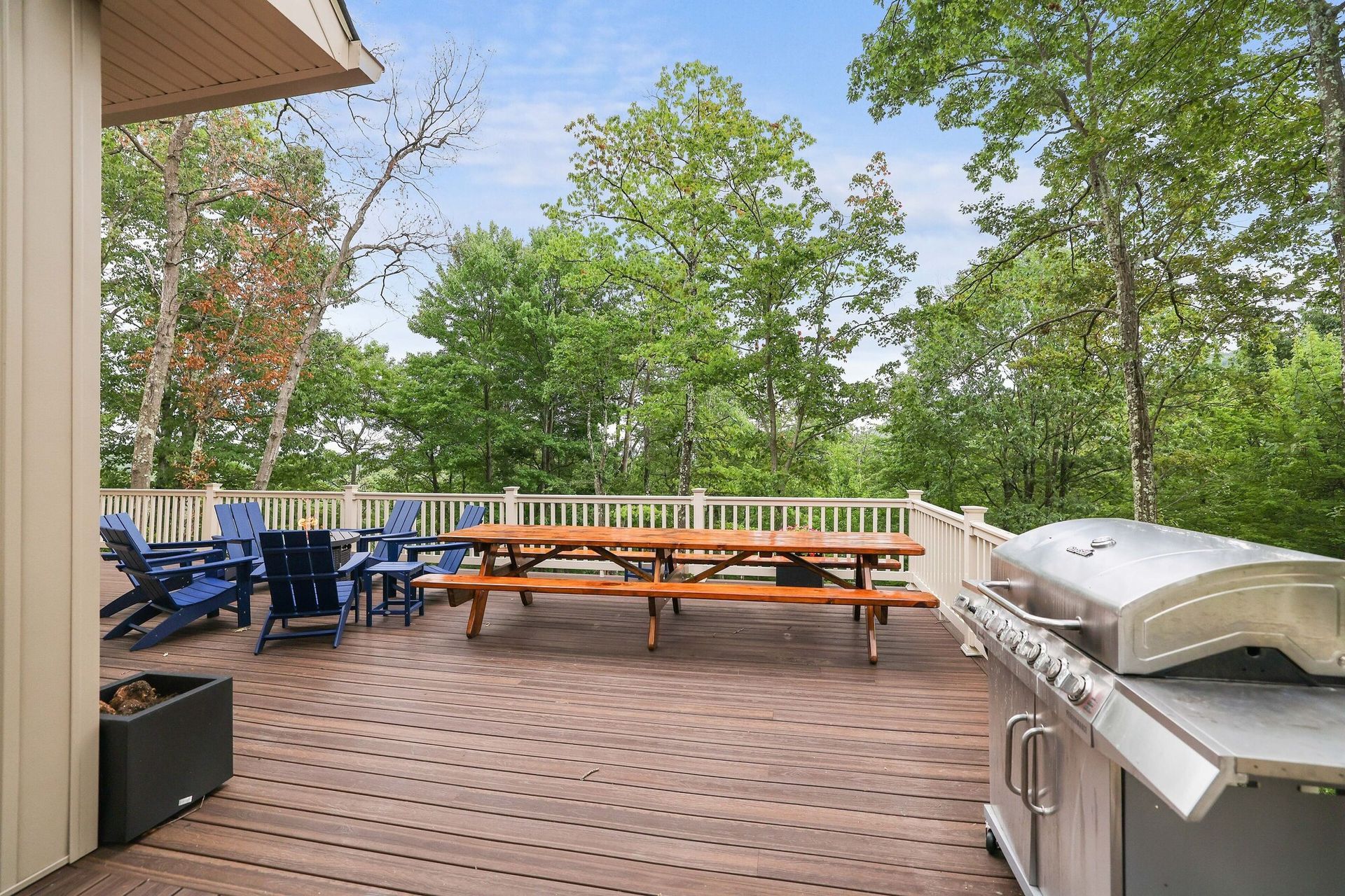 A large wooden deck with a picnic table and chairs and a grill.