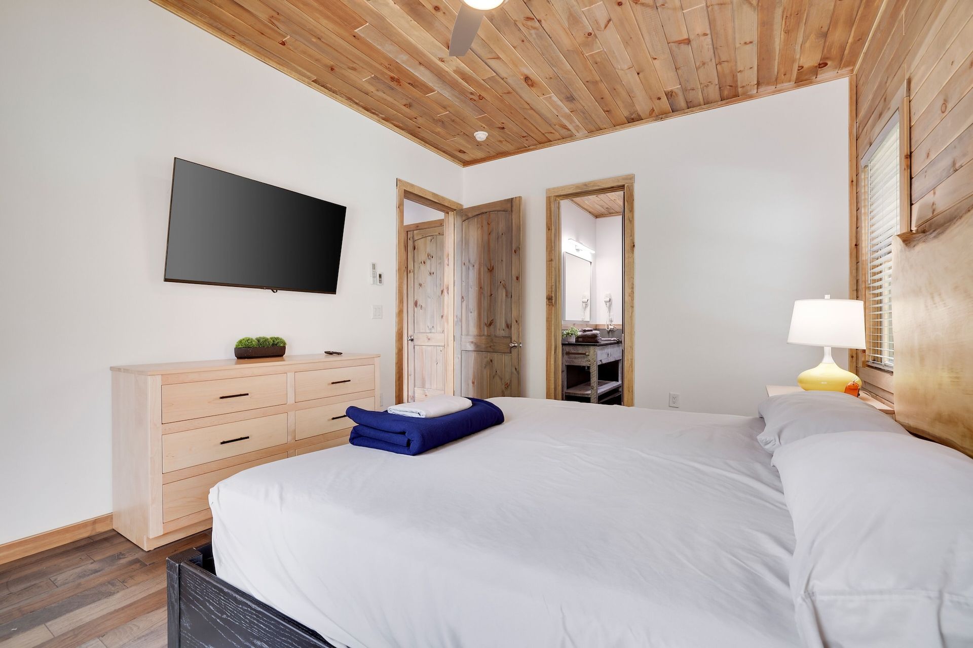 A bedroom with a bed , dresser , television and wooden ceiling.