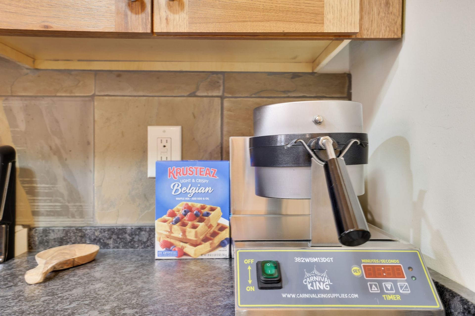 A waffle maker is sitting on a kitchen counter next to a box of waffles.